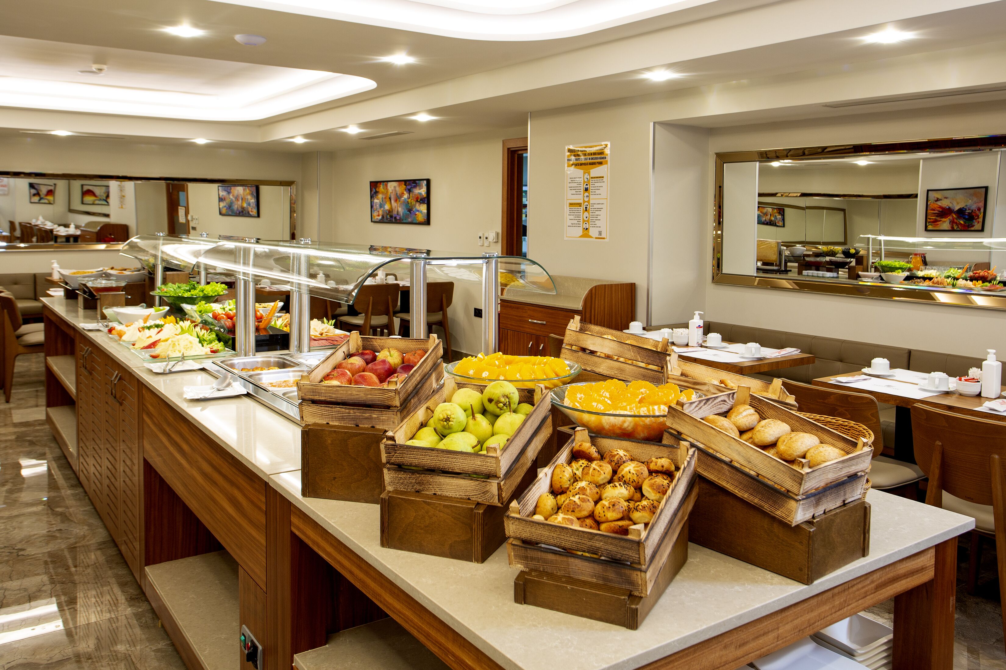 Buffet com diversos alimentos em cestos de madeira, um espelho e uma área de estar com mesas e cadeiras.