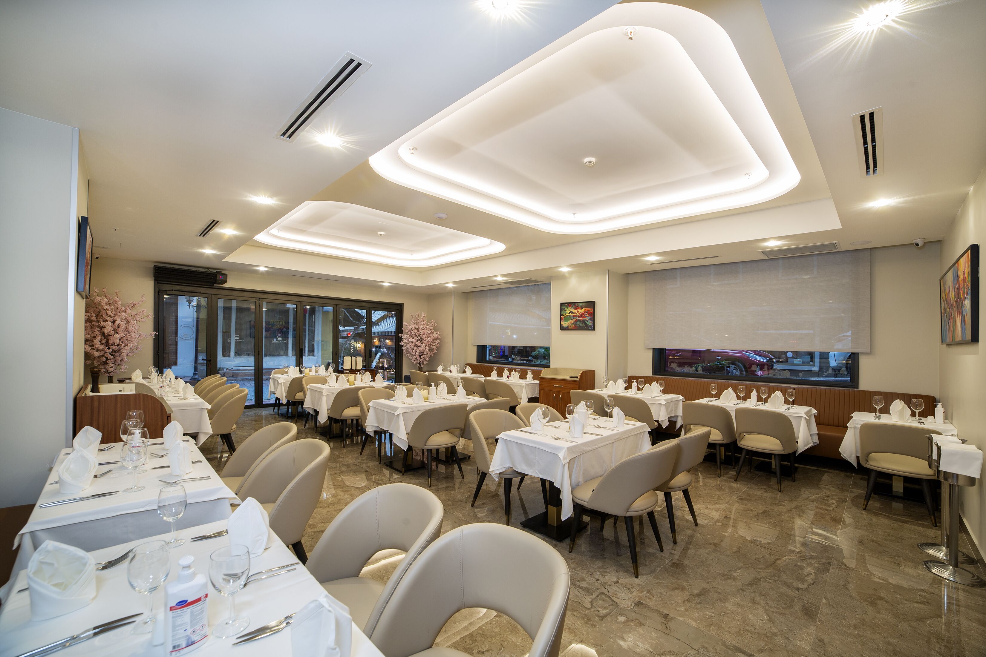 A restaurant with multiple tables set for dining, featuring a modern ceiling design and a large window with a view.