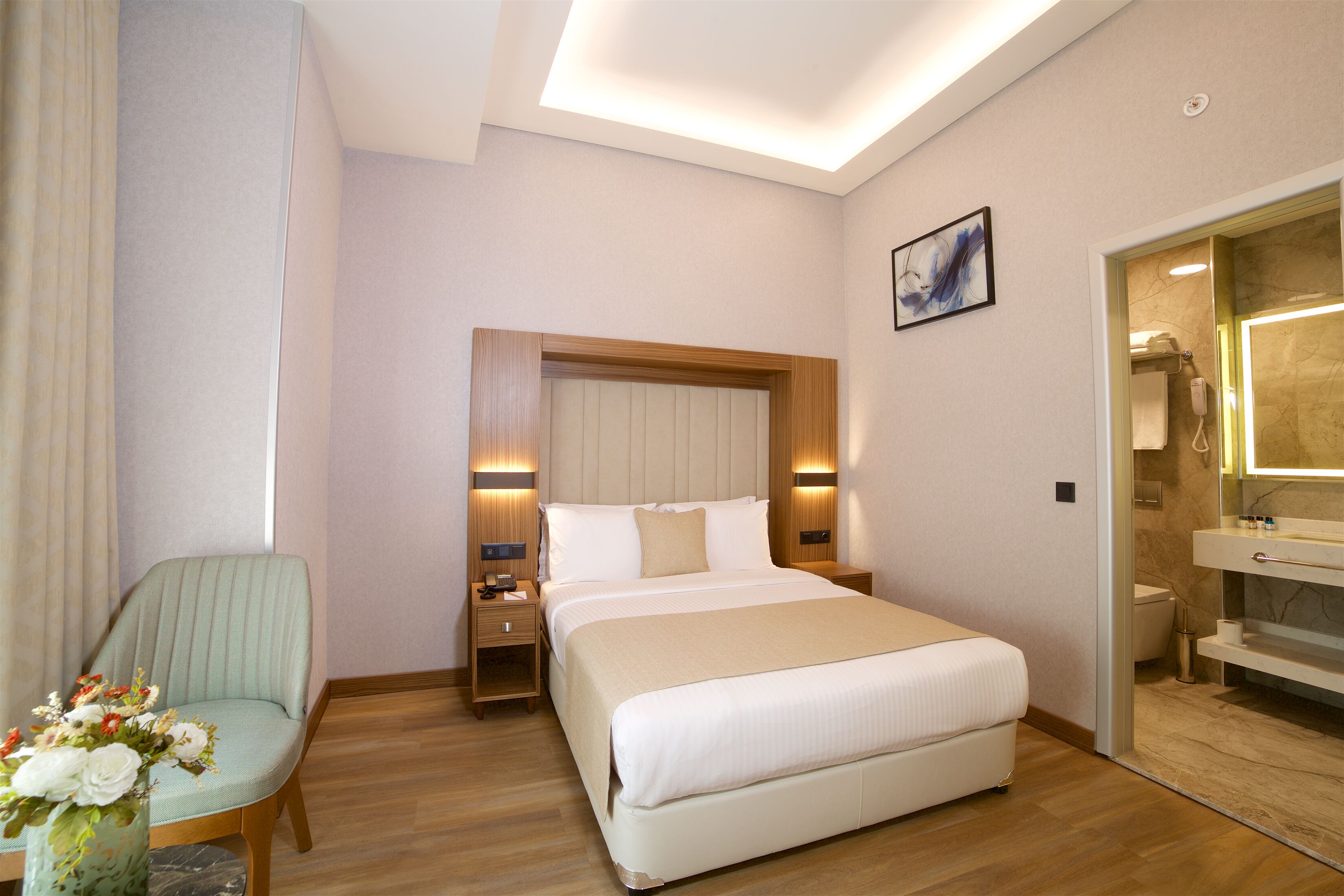 A hotel room with a bed, bedside table, chair, and a bathroom with a mirror and sink.