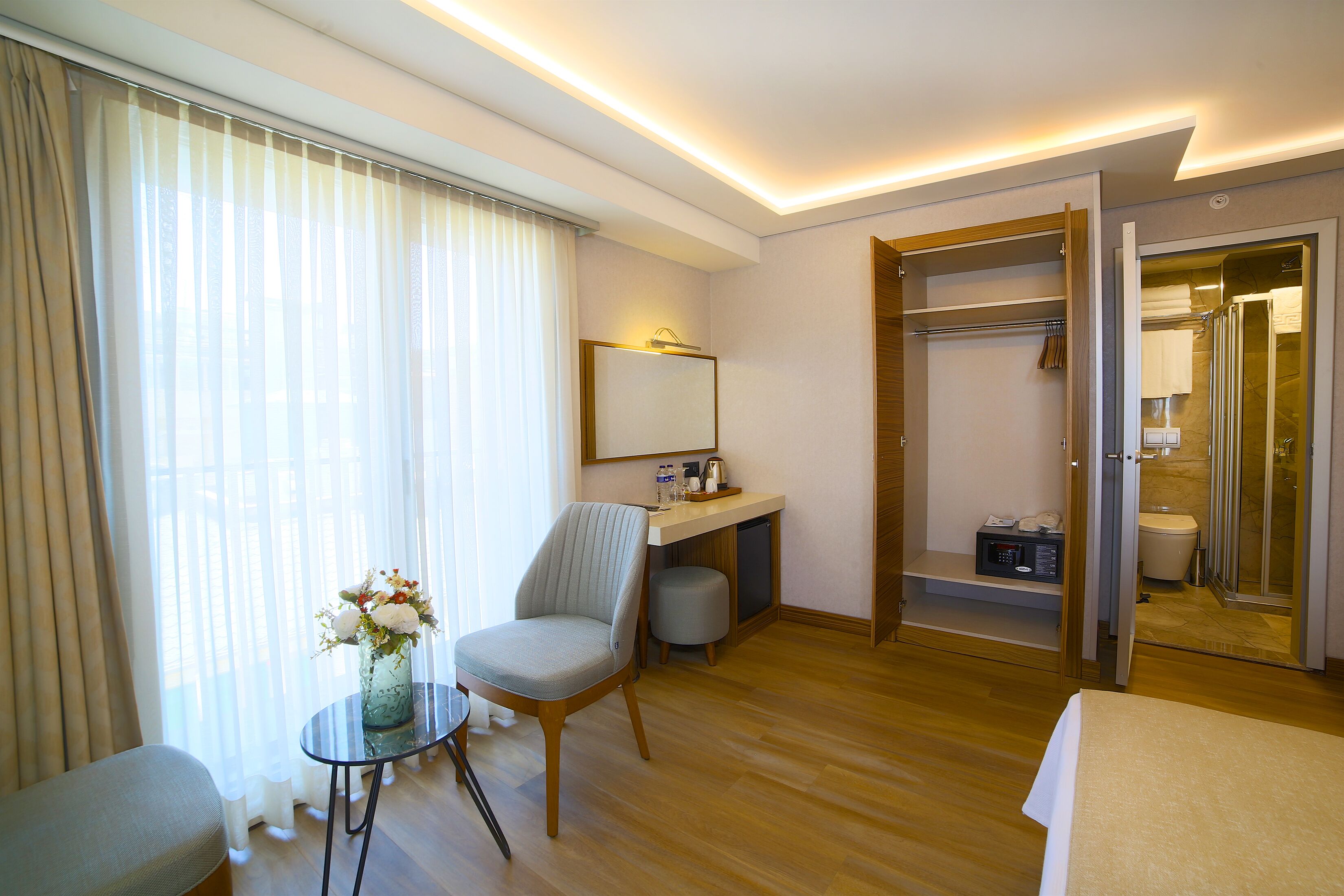 Une chambre d’hôtel comprenant un lit, un bureau, une chaise, une petite table avec un vase et une armoire.