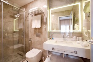 Un baño moderno con ducha de vidrio, lavamanos blanco y un espejo grande.