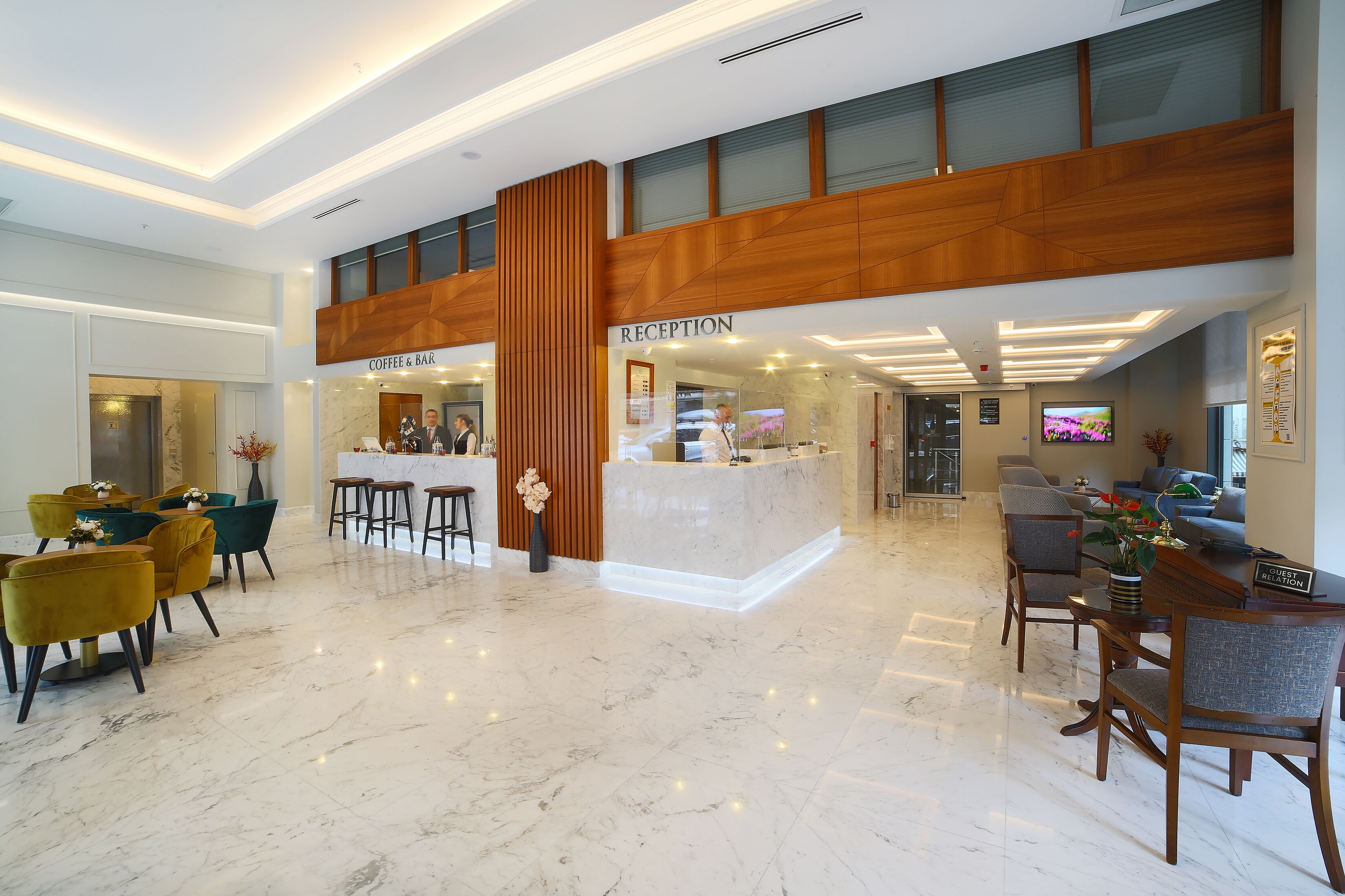Zona de recepción de un hotel con suelo de mármol, mostrador de madera y un bar de café.