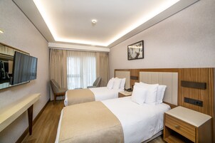 Habitación de hotel con dos camas, televisión, escritorio y un amplio ventanal con cortinas.