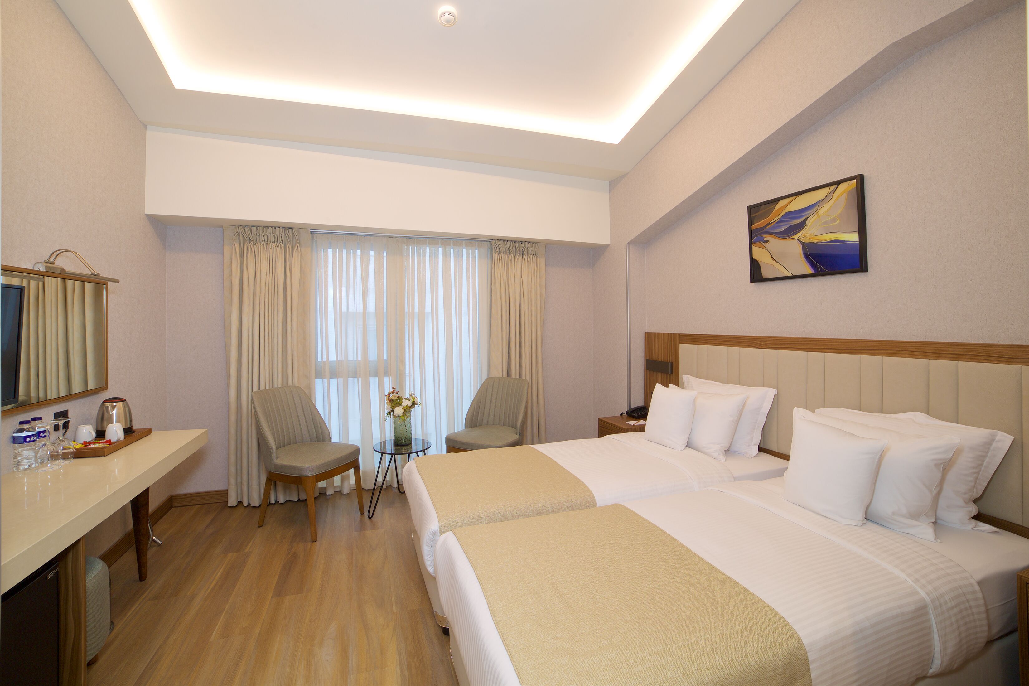 A hotel room with two beds, a desk with a computer, a chair, and a small table with a vase.