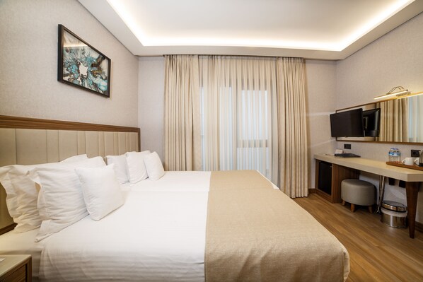 A hotel room with a large bed, a desk with a television, and a small trash can.