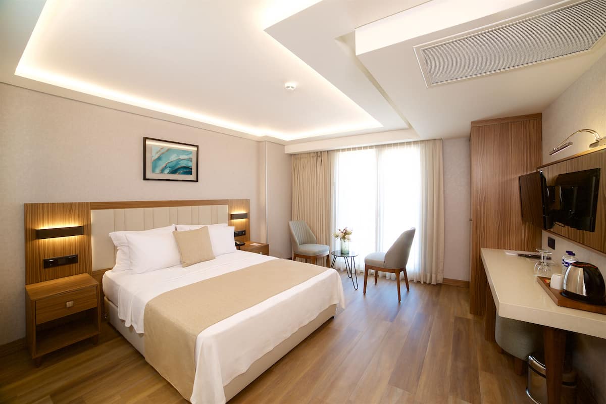 A hotel room with a large bed, bedside tables, a desk, a chair, and a television.