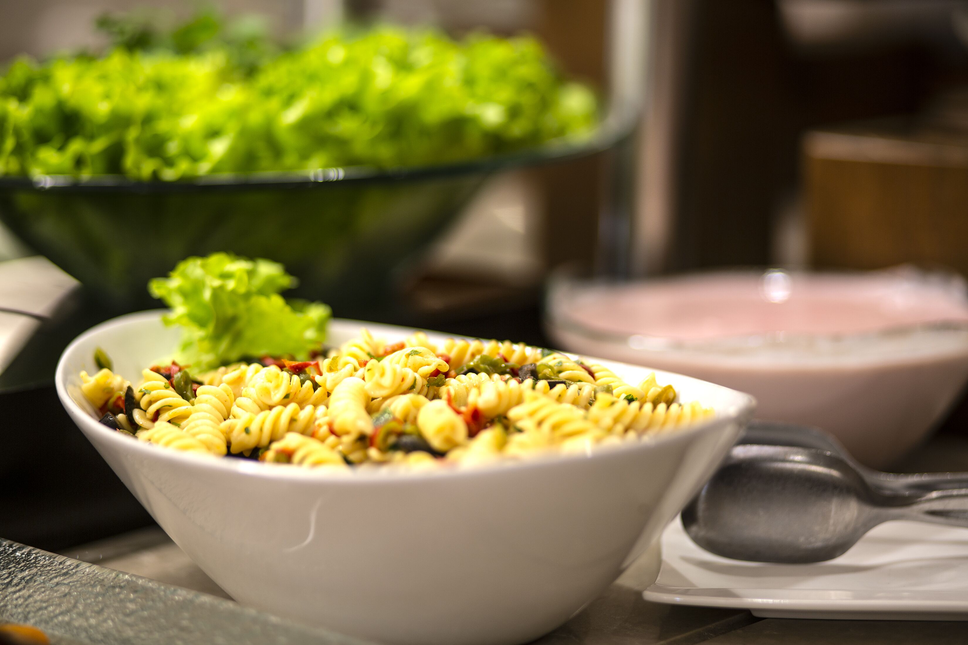 A bowl of pasta salad with a spoon and a bowl of green salad in the background.