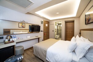 Habitación de hotel con cama, escritorio con televisor, cafetera y refrigerador pequeño.