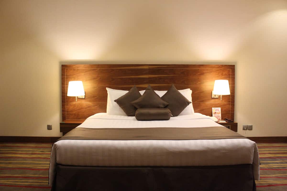 A hotel room with a large bed, two bedside lamps, a wooden headboard, and a striped carpet.