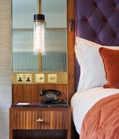 Una habitación con una cama, una mesita de noche con teléfono y una lámpara fijada en la pared.