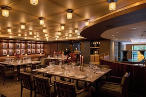 A restaurant with multiple tables set for dining, a bar area, and framed pictures on the walls. - The Fitzwilliam Hotel (Dublin)