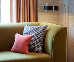 A sofa with two pillows, a lamp, and a window with curtains.