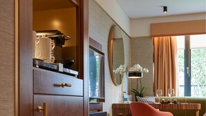 Une chambre moderne avec une armoire en bois, un grand miroir, une chaise rose, une table à manger agrémentée d’un vase de fleurs et une fenêtre avec des rideaux.