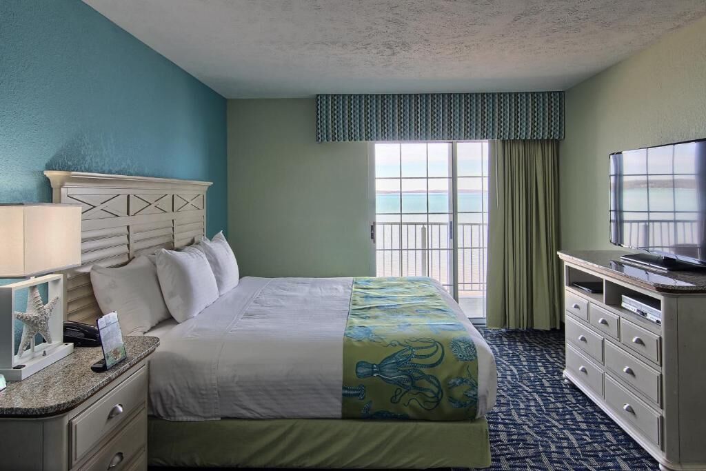 Una habitación de hotel con cama, televisor, cómoda y ventana con vista al mar.