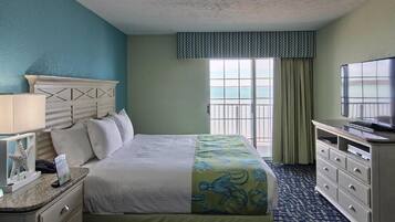 A hotel room with a bed, a television, a dresser, and a window with a view of the sea.