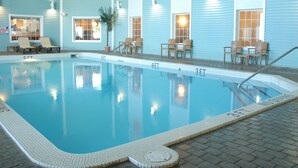 Piscina interior com água cristalina, rodeada por espreguiçadeiras e um deck revestido de azulejos.
