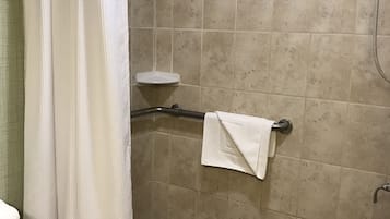A shower area with a white shower curtain, a handheld showerhead, a grab bar, a small white shelf, and a towel rack with a towel.