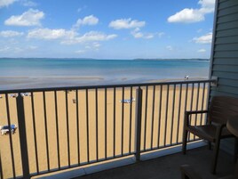 Un balcón con vista a la playa, una silla y una mesa.