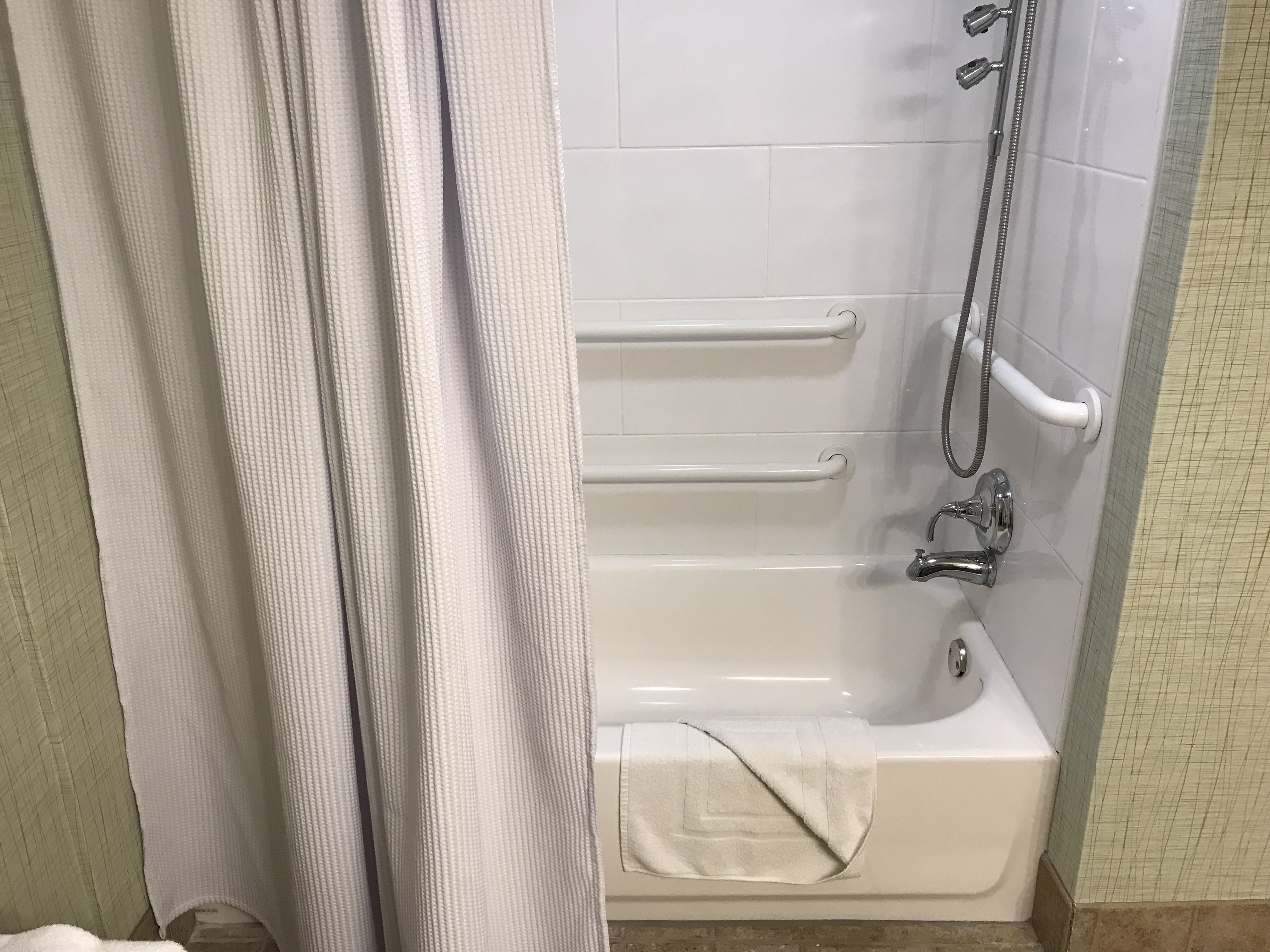 A bathroom with a bathtub, grab bars, a showerhead, and a towel.