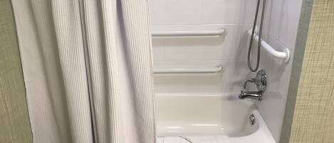 A bathroom with a bathtub, grab bars, a showerhead, and a towel.