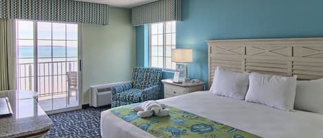 A hotel room with a large bed, a desk, a chair, and a view of the ocean through the sliding doors.
