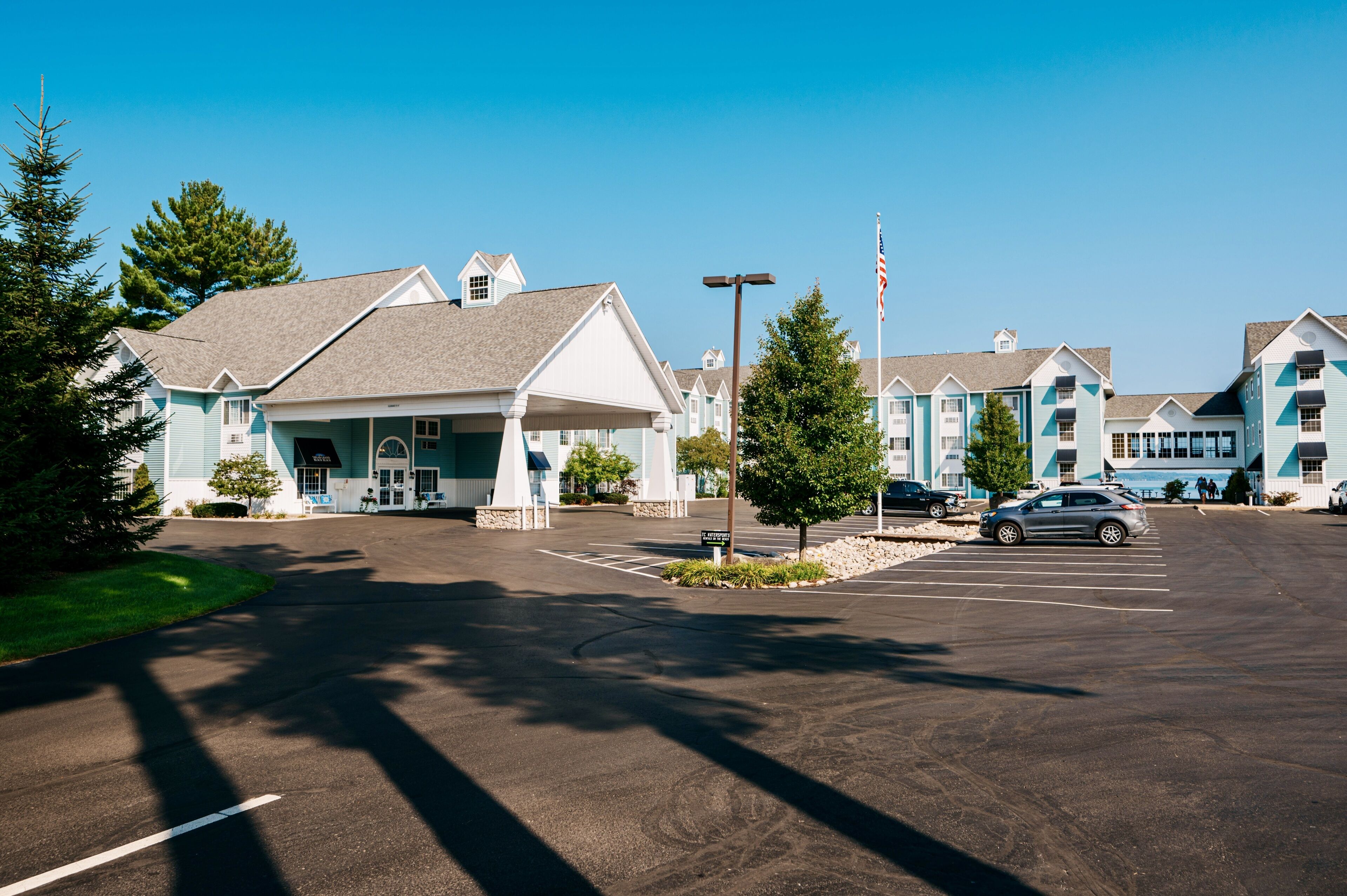 A parking lot with several buildings, including a hotel with a covered entrance and a flagpole.