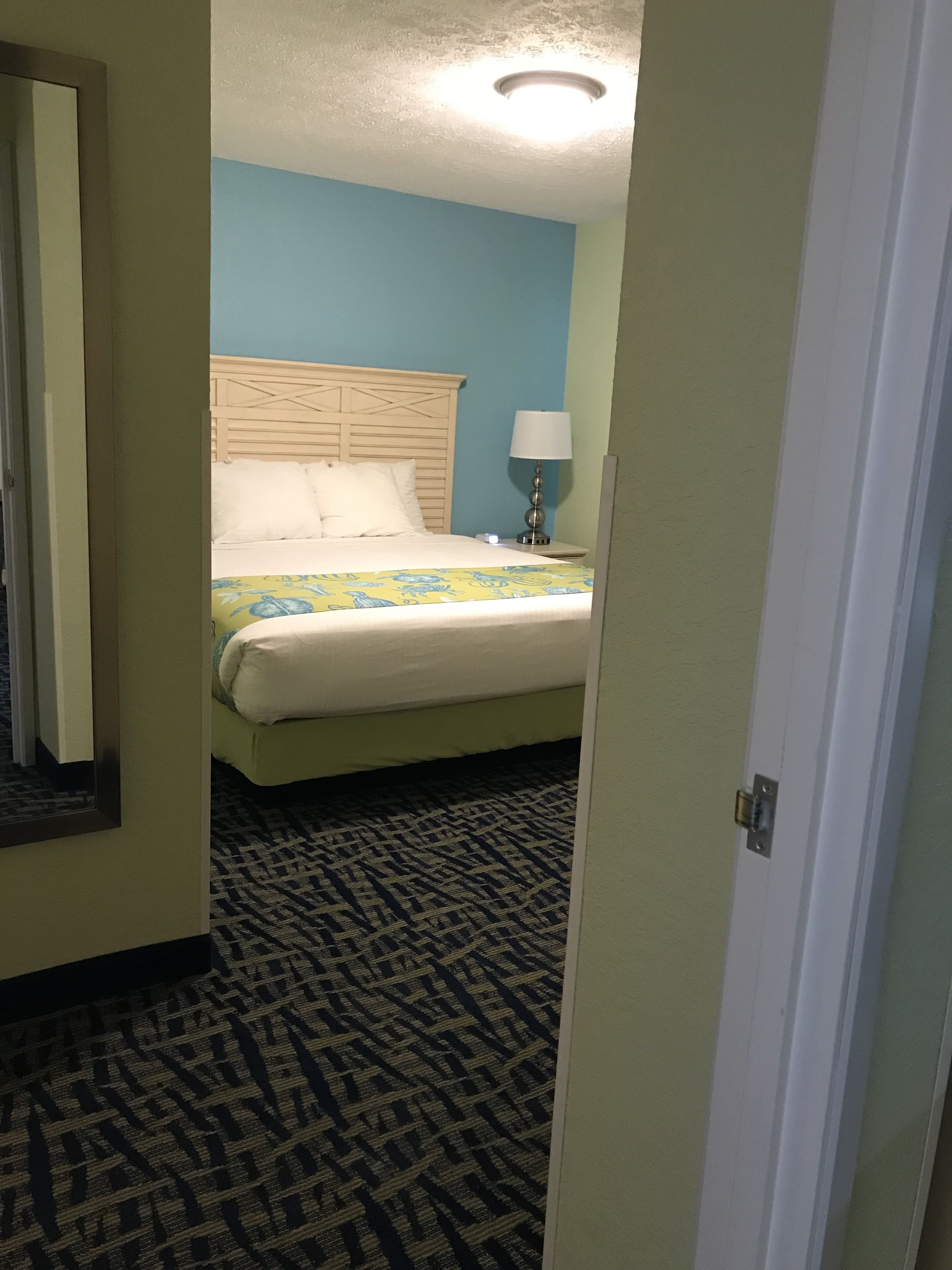 A hotel room with a bed, a nightstand, a lamp, and a patterned carpet.