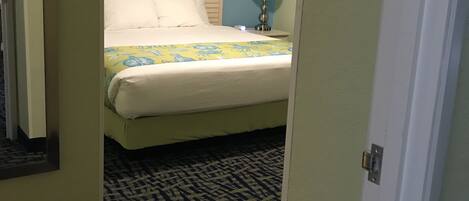 Una habitación de hotel con una cama, una mesita de noche, una lámpara y una alfombra estampada.