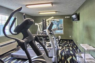 Un gimnasio con cintas de correr, elípticas y un televisor en la pared.