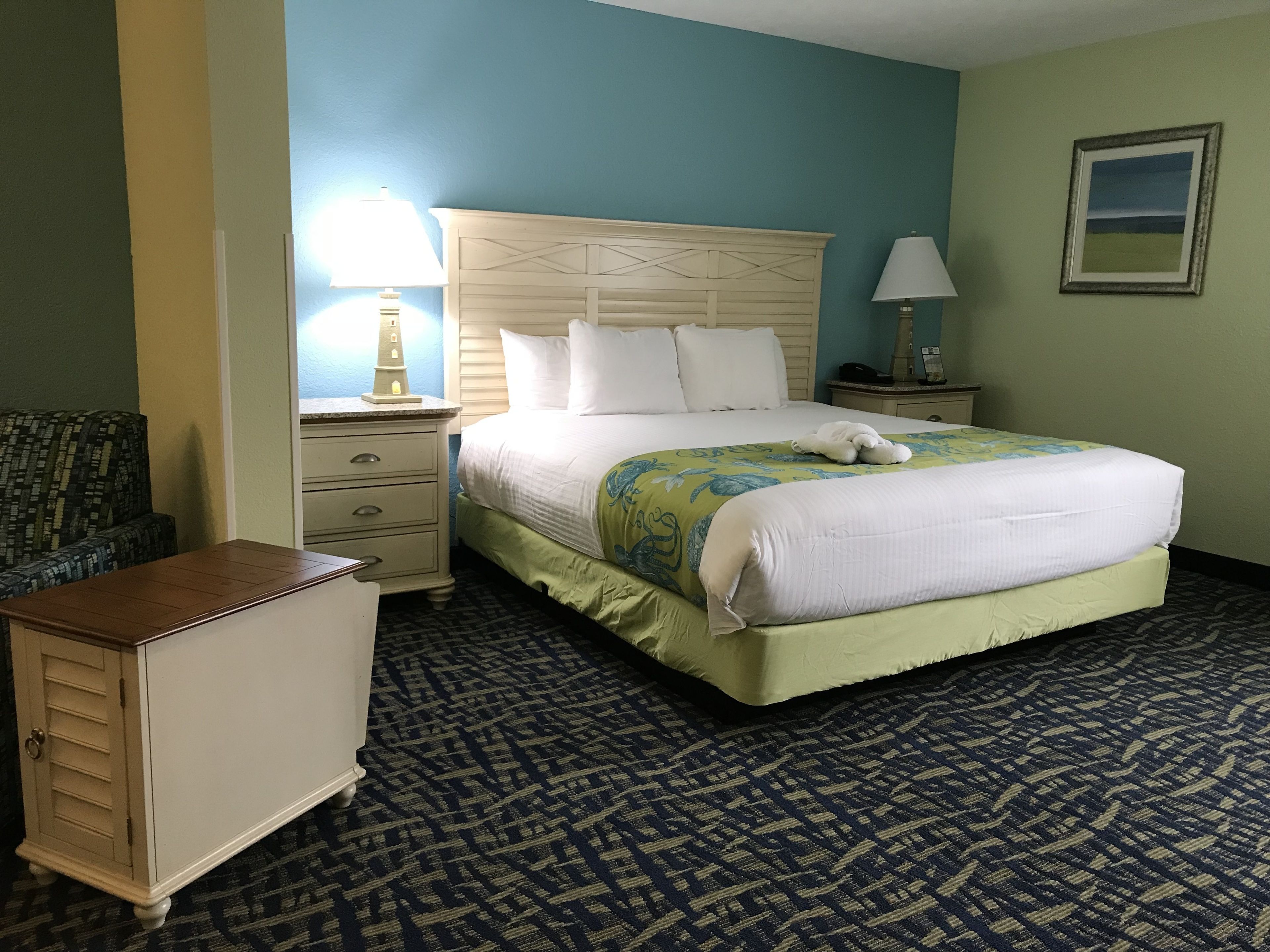A hotel room with a large bed, a nightstand, a dresser, and a chair.