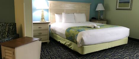 A hotel room with a large bed, a nightstand, a dresser, and a chair.