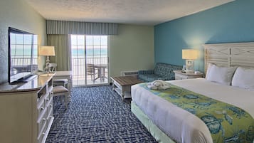 A hotel room with a large bed, a desk, a chair, a TV, and a view of the ocean through the window.