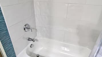 A bathroom with white tiles, a bathtub, and a sink.
