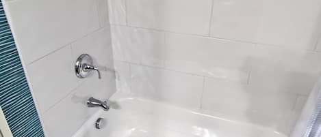 A bathroom with white tiles, a bathtub, and a sink.