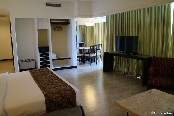 A hotel room with a bed, a desk, a TV, and a dining area.