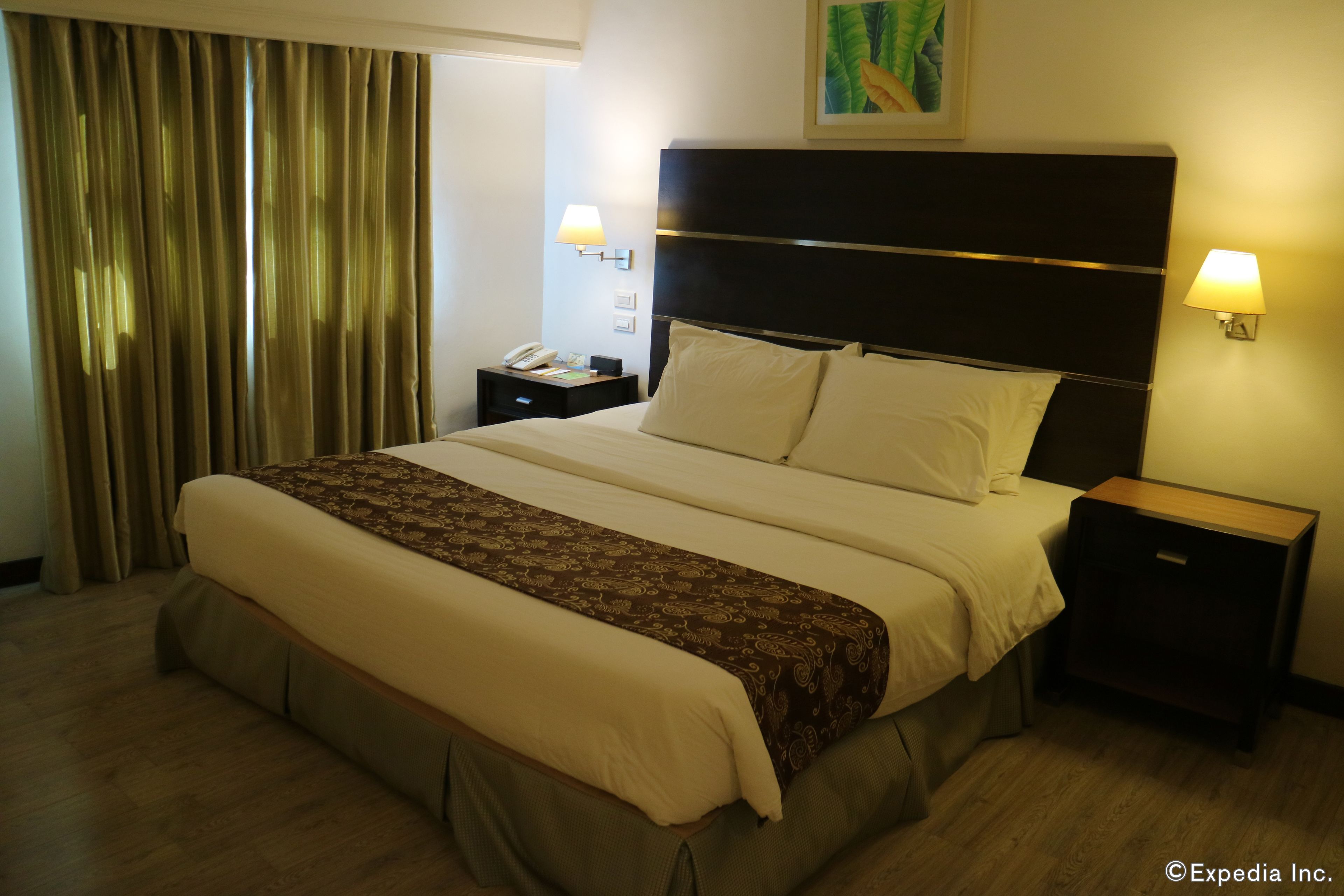 Habitación de hotel con una cama grande, dos mesitas de noche, una lámpara y un cuadro en la pared.