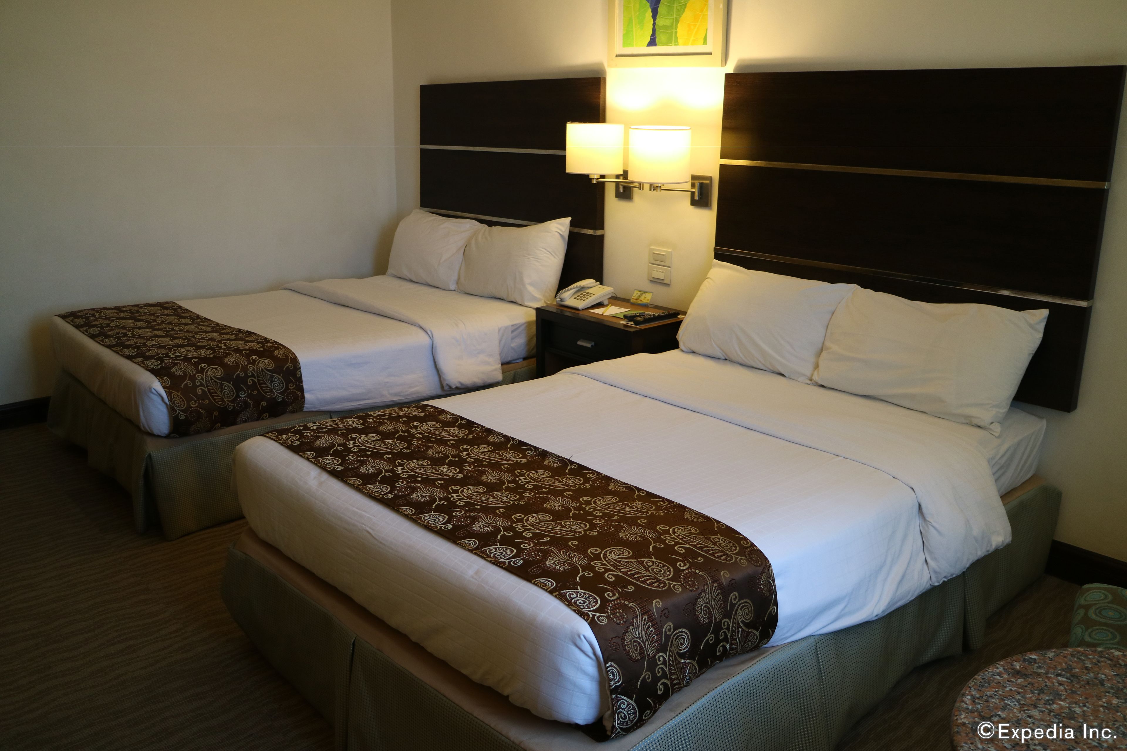 A hotel room with two beds, each with a patterned bedspread and white pillows. There is a nightstand with a lamp and a telephone.