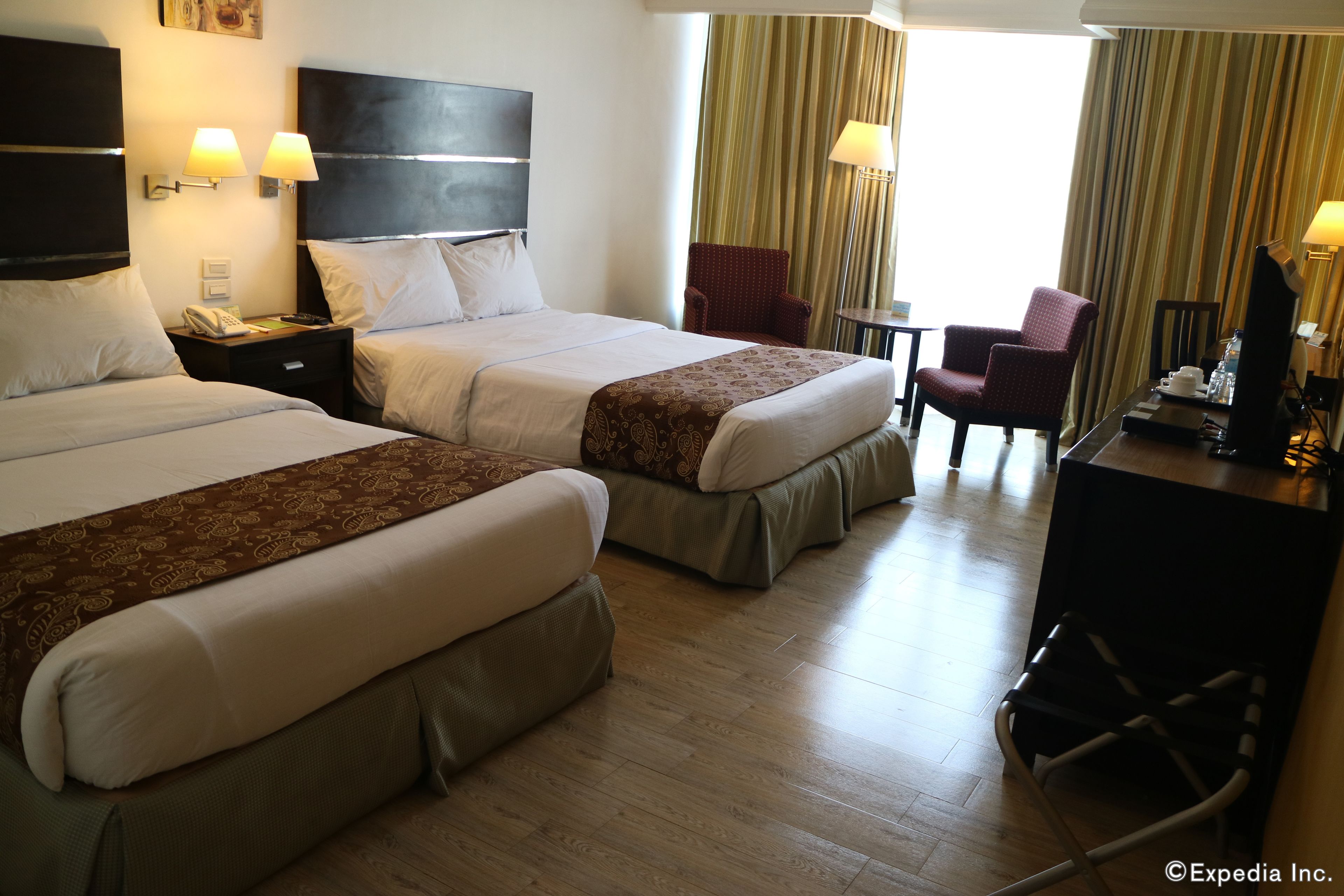 Quarto de hotel com duas camas, uma escrivaninha, uma cadeira e uma televisão.