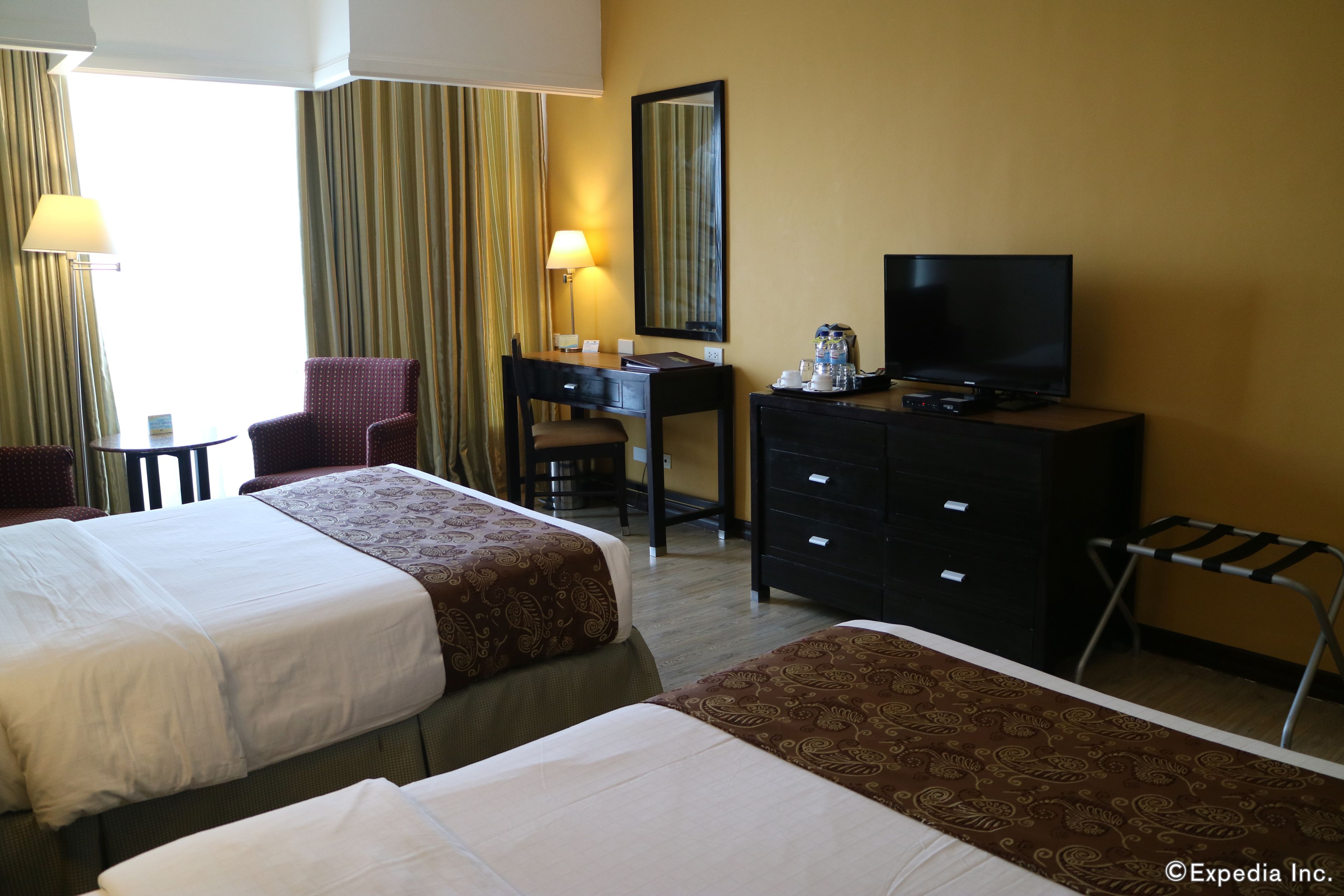 A hotel room with two beds, a desk, a television, and a dresser.