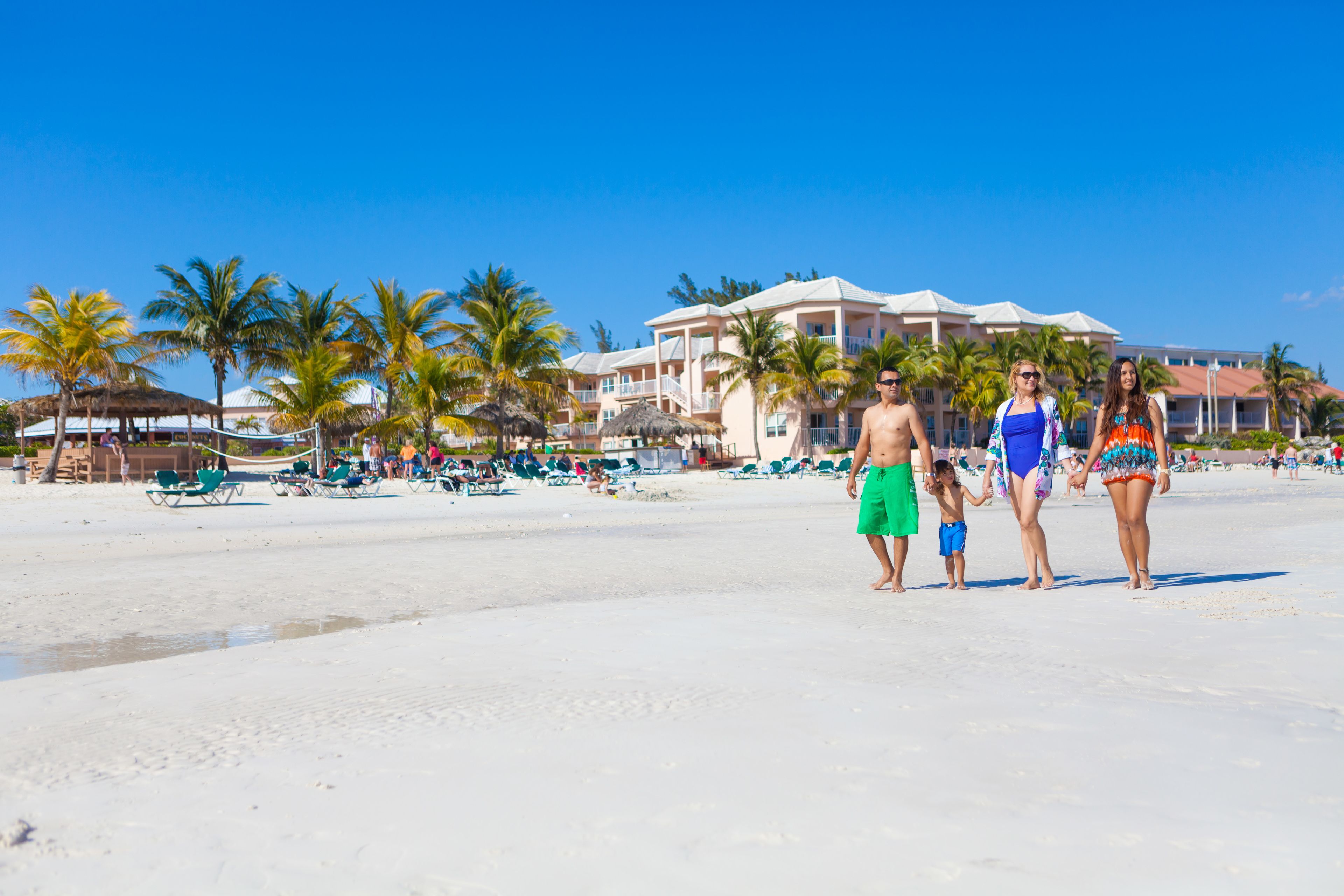 Un resort en la playa con un edificio grande, palmeras y sillas de playa.