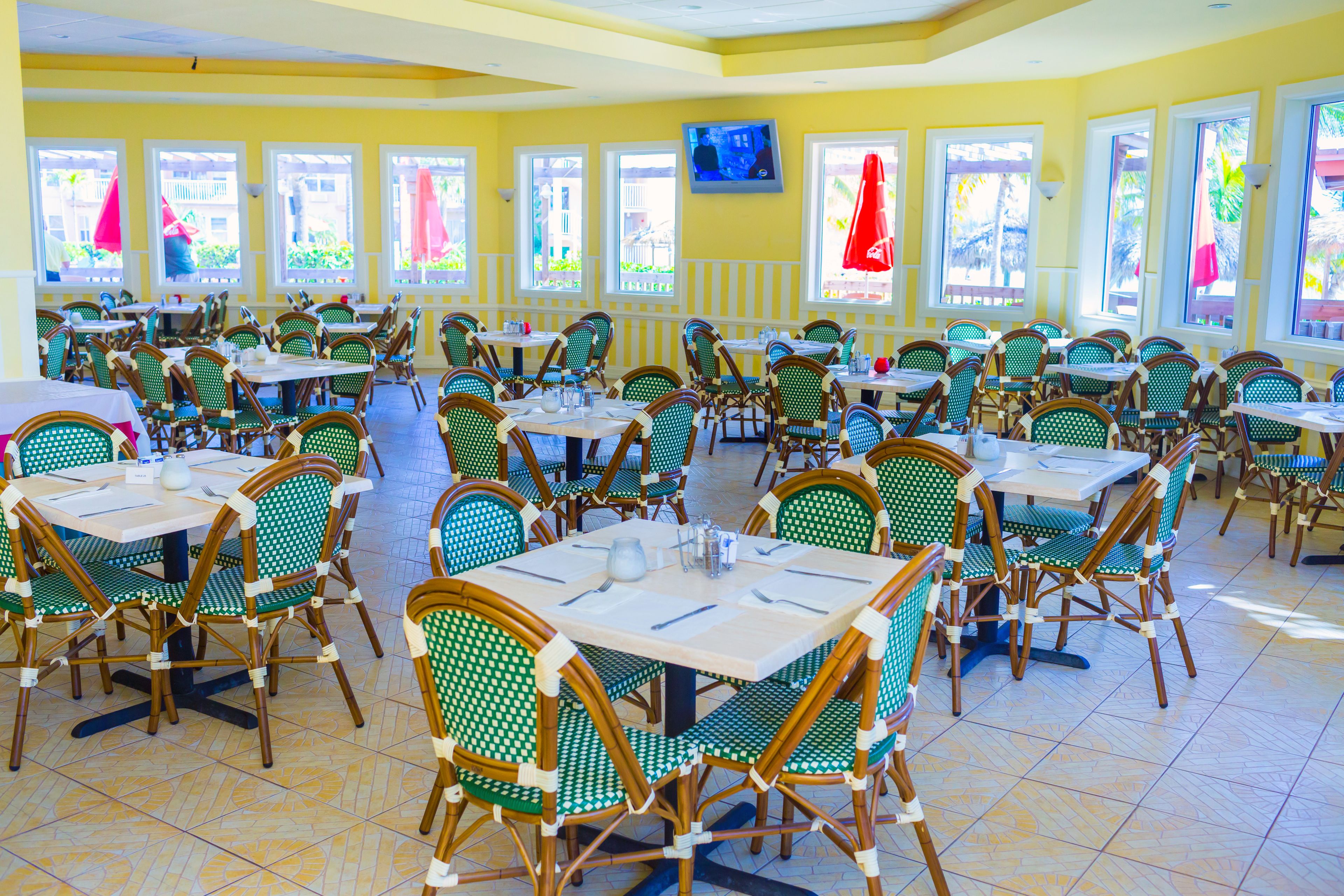 A restaurant with multiple tables and chairs, large windows, and a television on the wall.