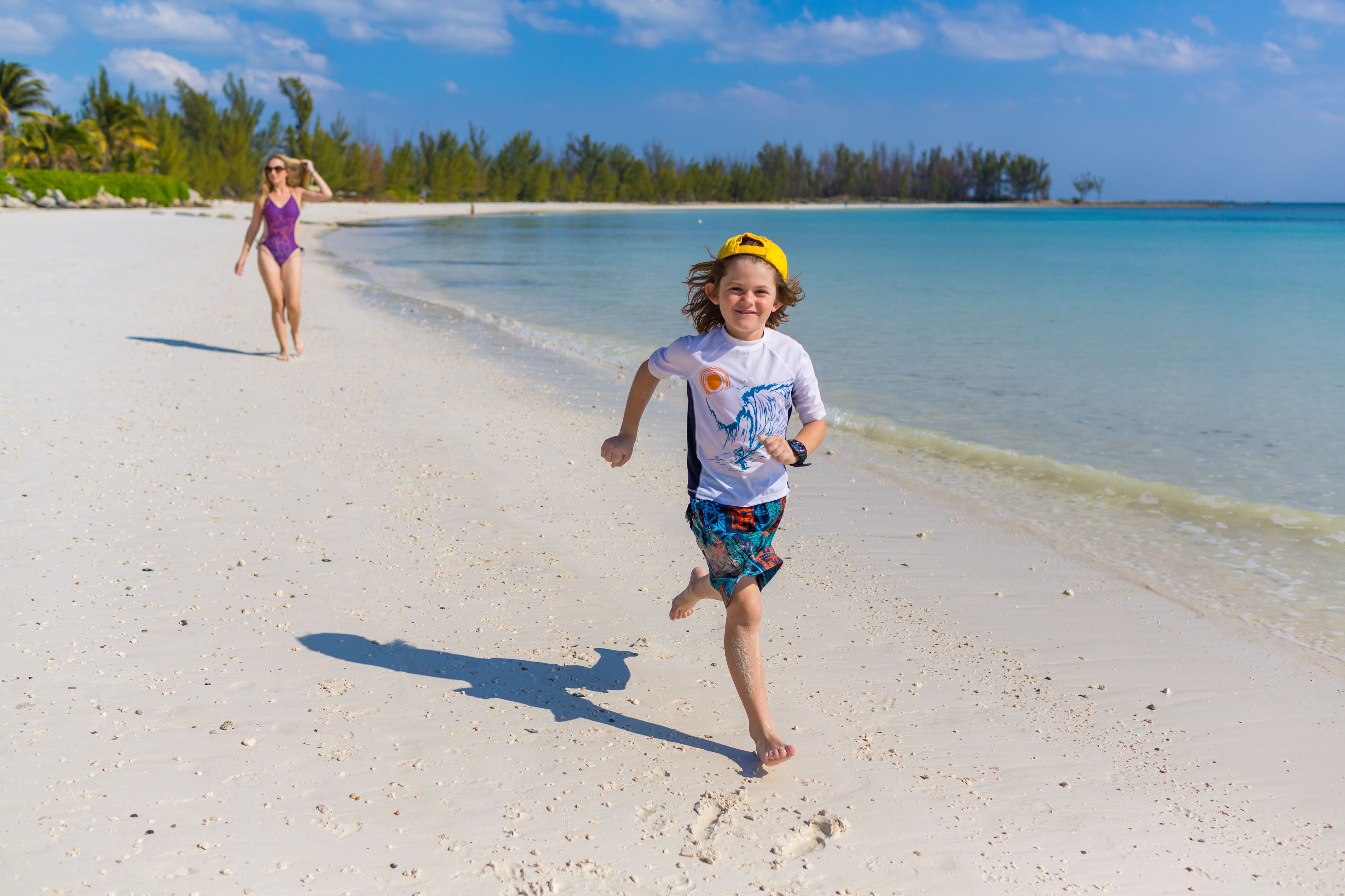 Una spiaggia con un bambino che corre verso l'acqua e un adulto sullo sfondo.