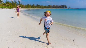 A beach scene with a child running towards the water and an adult in the background.