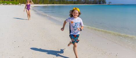 Una spiaggia con un bambino che corre verso l'acqua e un adulto sullo sfondo.
