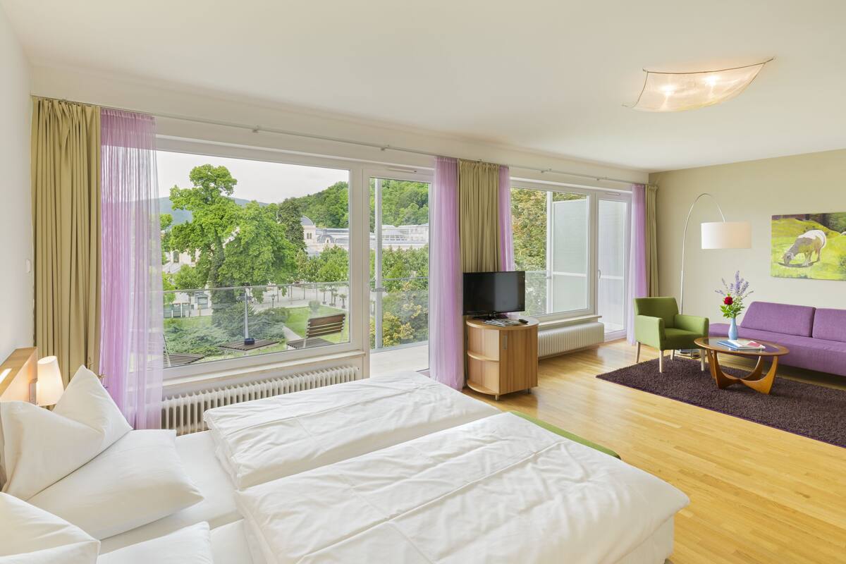 Ein Hotelzimmer mit einem großen Bett, einem Fernseher, einer Couch und Blick auf Grünflächen.