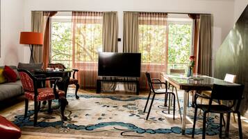 A living room with a sofa, TV, dining table, chairs, and a large window with curtains.