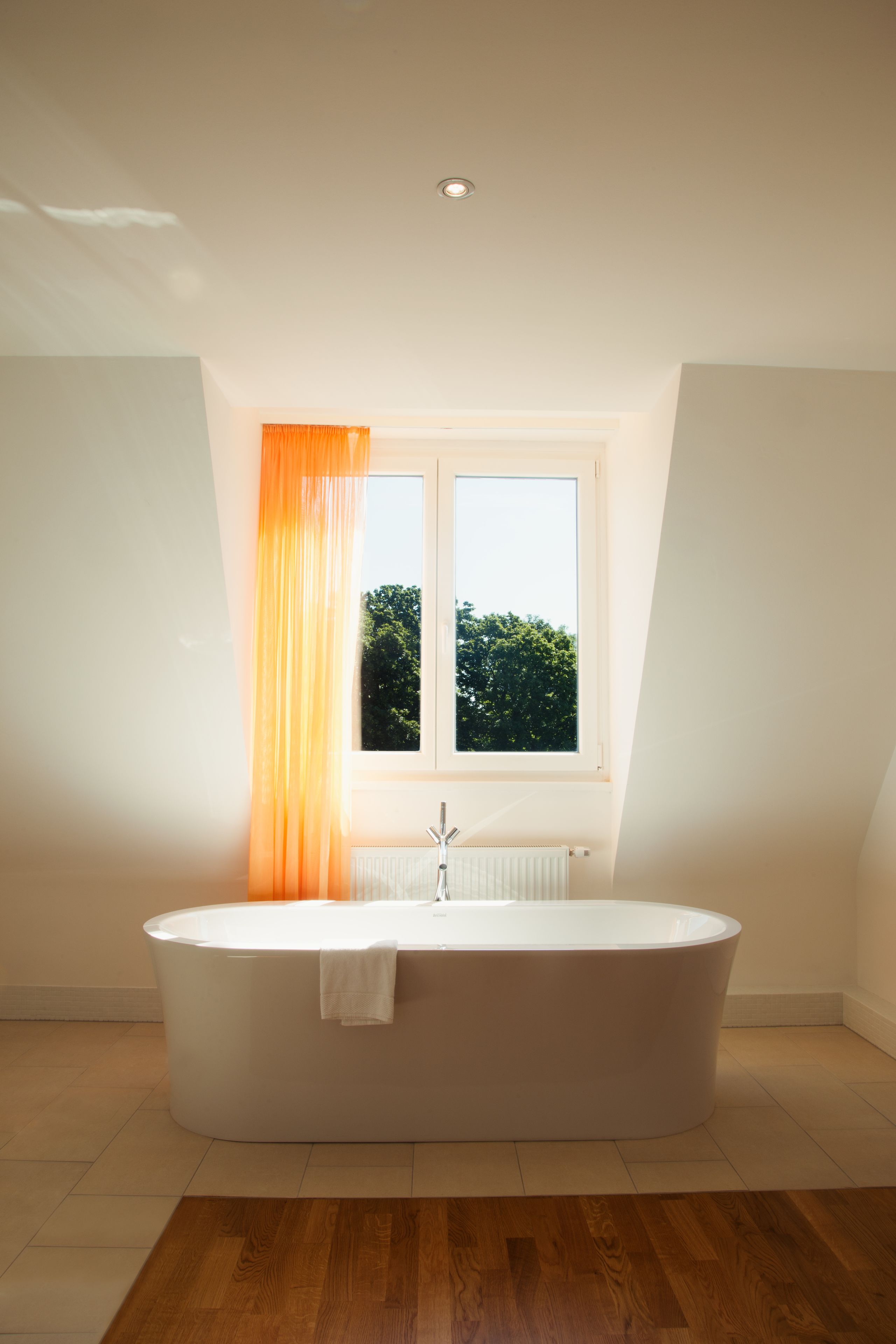 Un bagno moderno con una vasca da bagno indipendente, una finestra con tende arancioni e vista su del verde all'esterno.