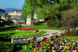 A park with benches, a flower garden, and a building with a dome and arched windows. - At the Park Hotel (Baden)
