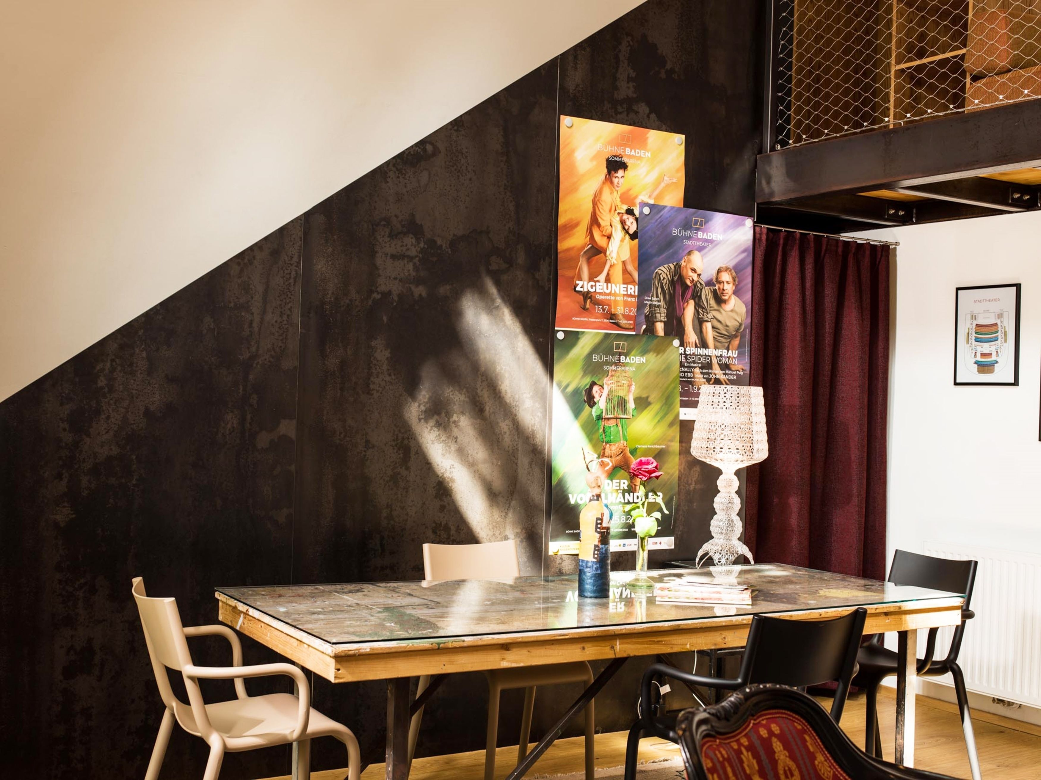 A dining area with a glass table, chairs, posters on the wall, and a lace table lamp.
