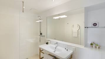 Un baño moderno con un espejo grande, ducha y tocador con lavabo.